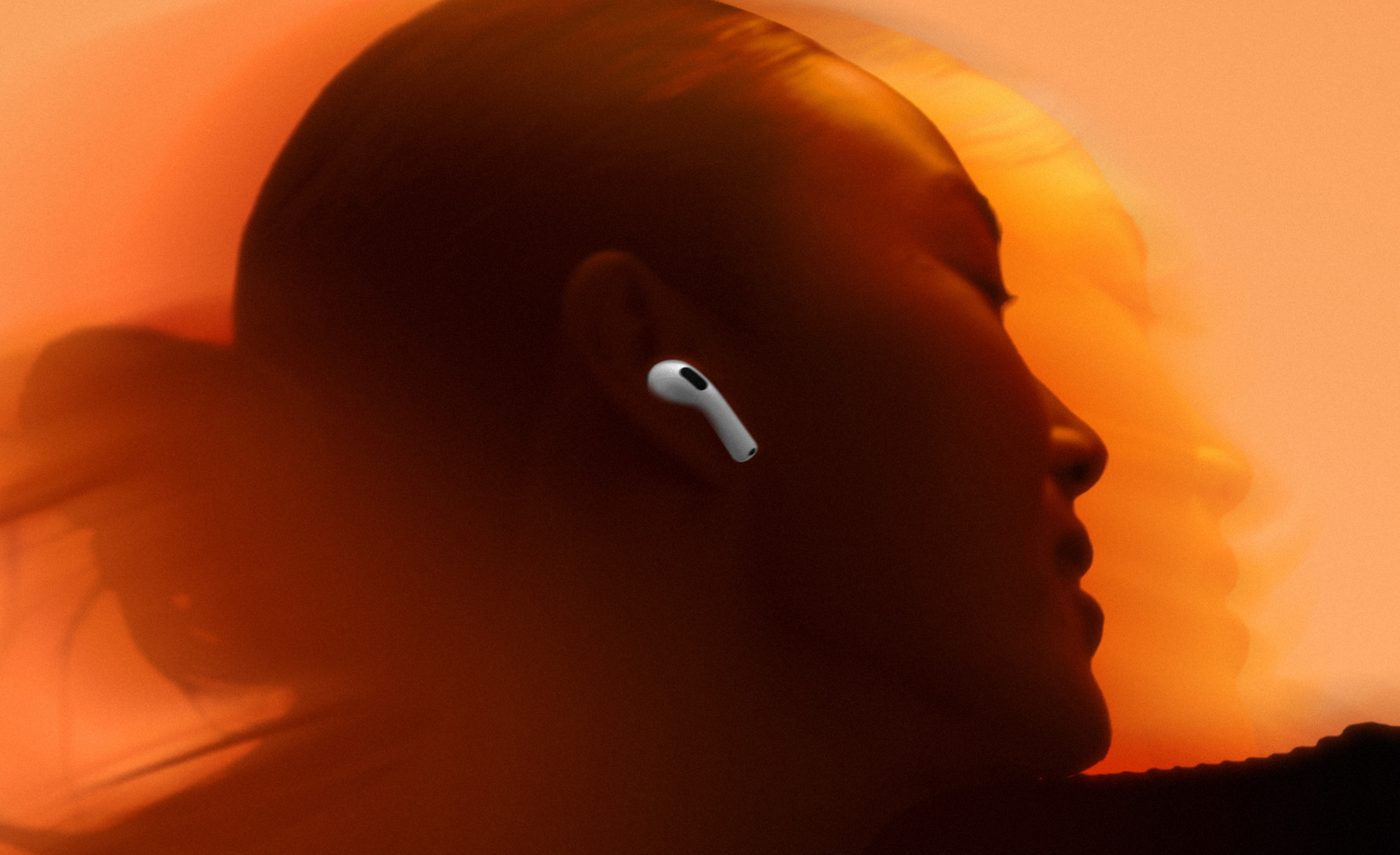 A person in profile wearing a white AirPods 5 earbud against an orange backdrop