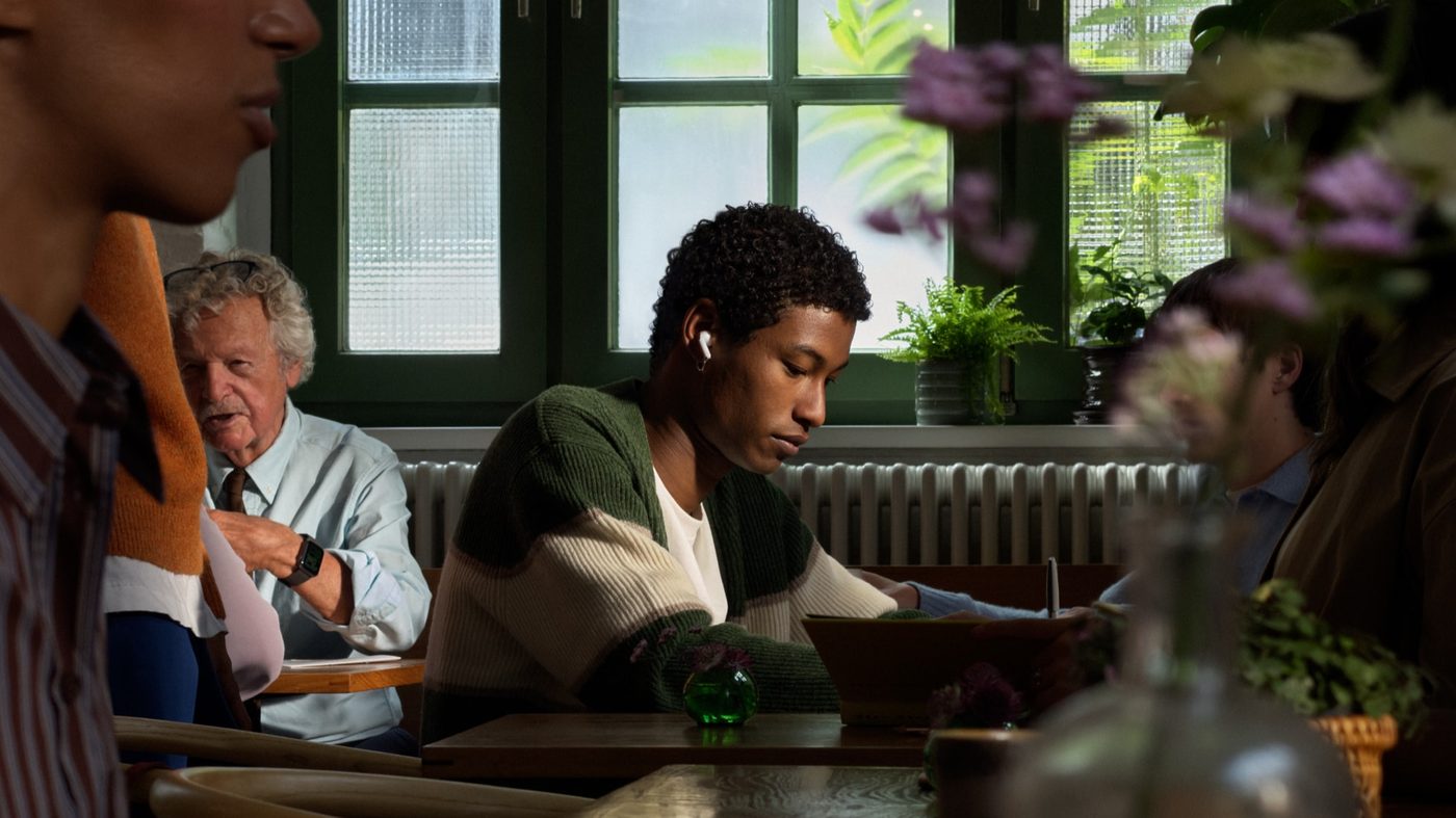 A cafe table, with a customer wearing AirPods 5 while writing
