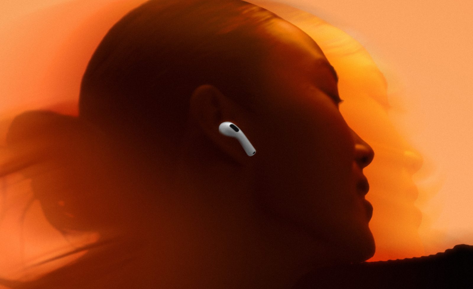 A person in profile wearing a white AirPods 5 earbud, against an orange sunset