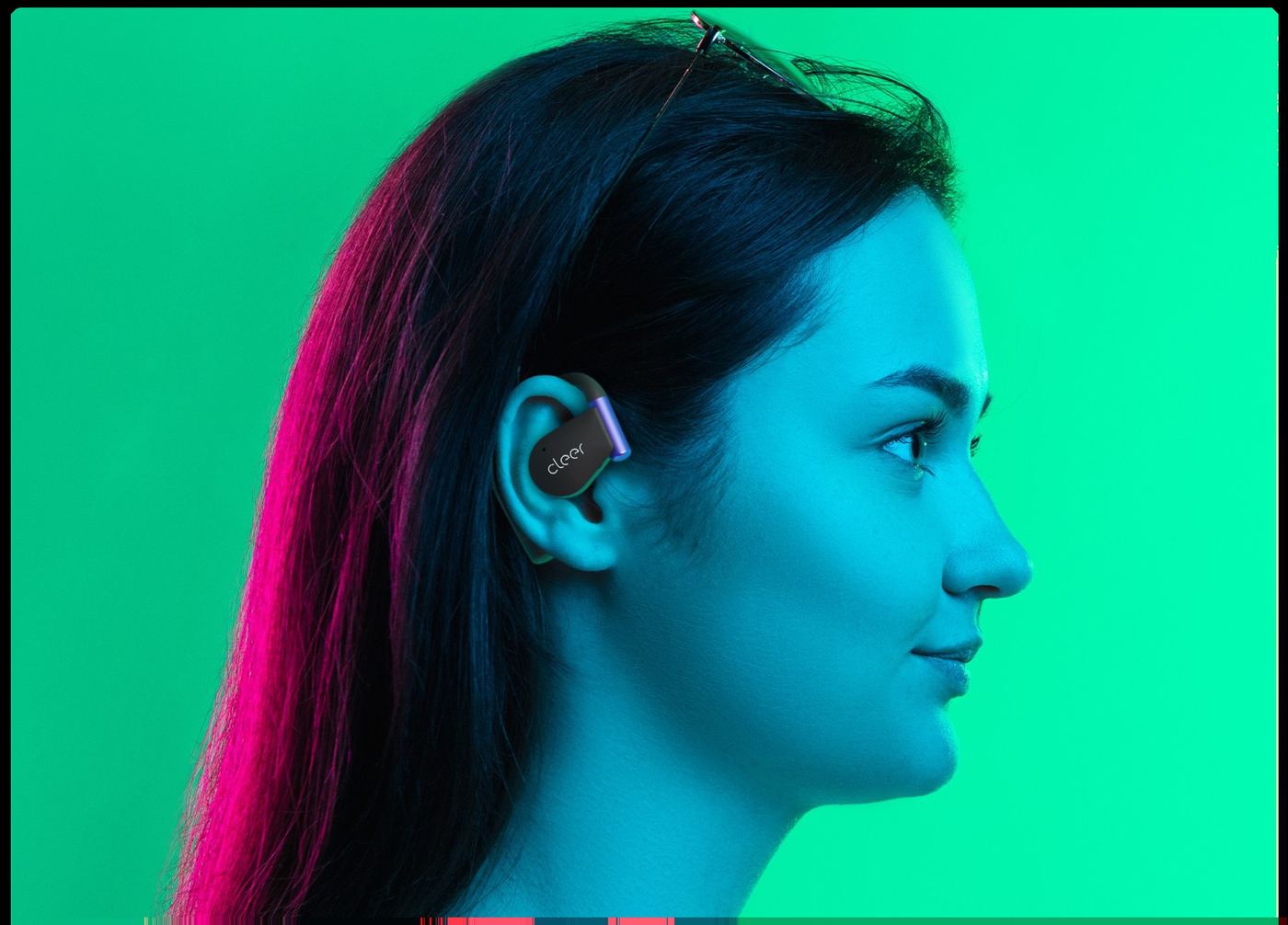 A person in a green shirt wearing gold Cleer ARC 5 Gaming earbuds