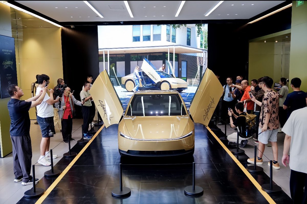 A gold Cybercab with doors open on a Tesla showroom floor as visitors take photos