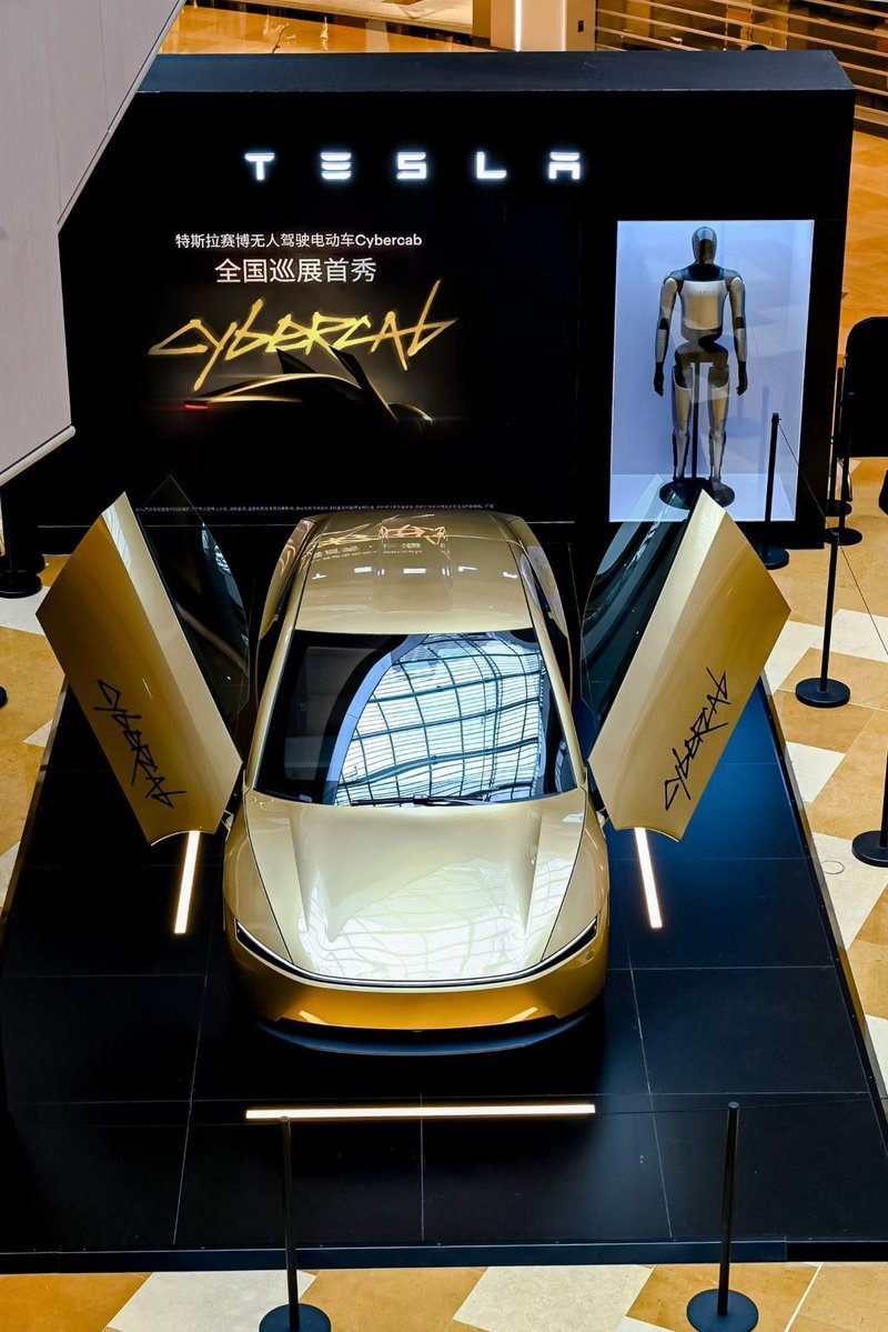 Overhead view of a gold Cybercab with both doors open at a Tesla mall display