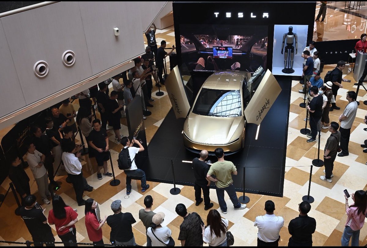Crowd around a Cybercab display in a Shanghai mall atrium, with an Optimus figure behind