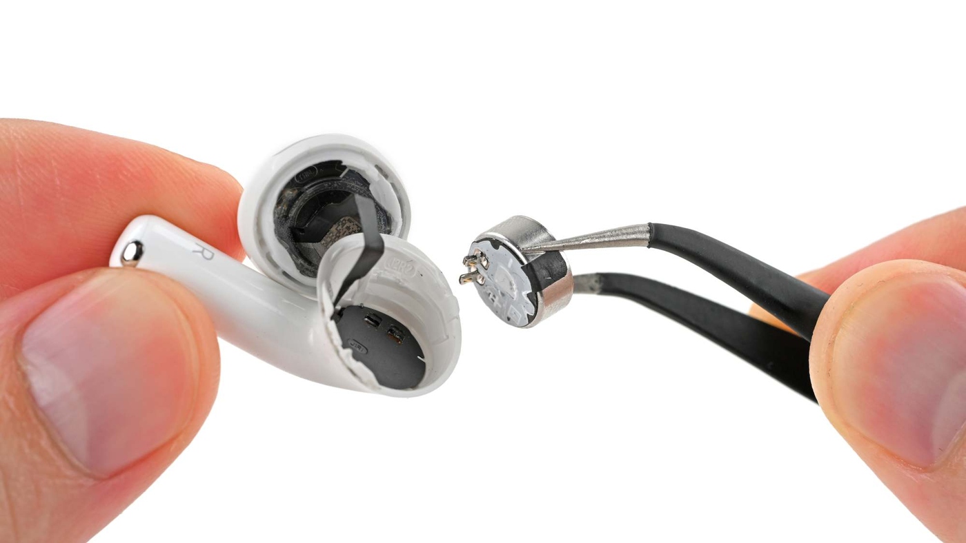 An AirPods 5 earbud opened around the driver, with its battery lifted out by tweezers, prongs attached