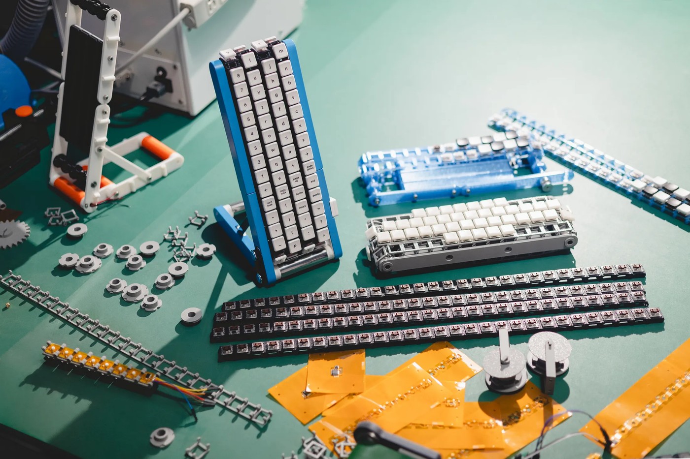 3D-printed frames, belt links, switches and circuit boards laid out for a home build.