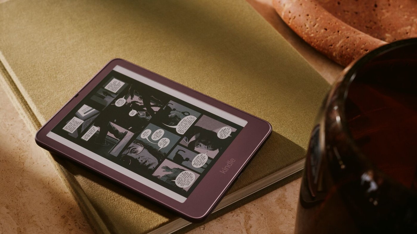 New Kindle Colorsoft in Fig showing a comic page, resting on a book