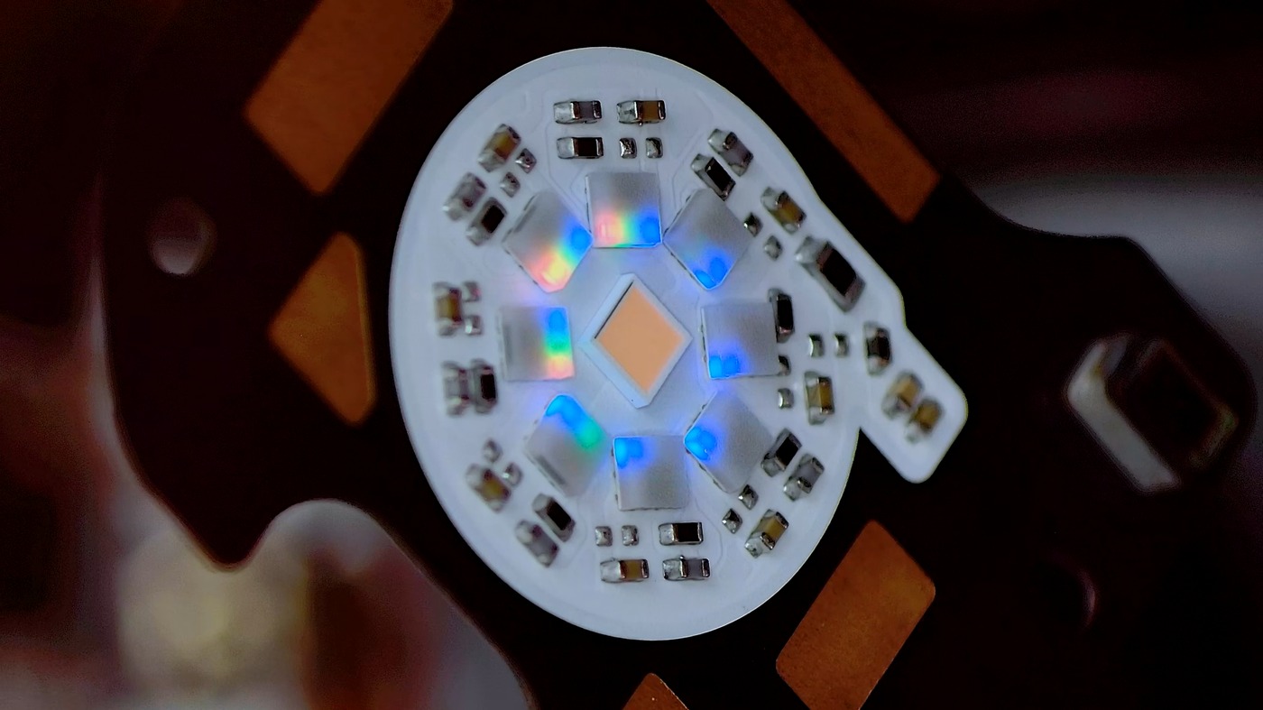 Close-up of the Pixel 11 Pro HiLight board with its diffuser removed: eight small LEDs, lit in mixed colors, arranged in a ring around the central camera flash LED