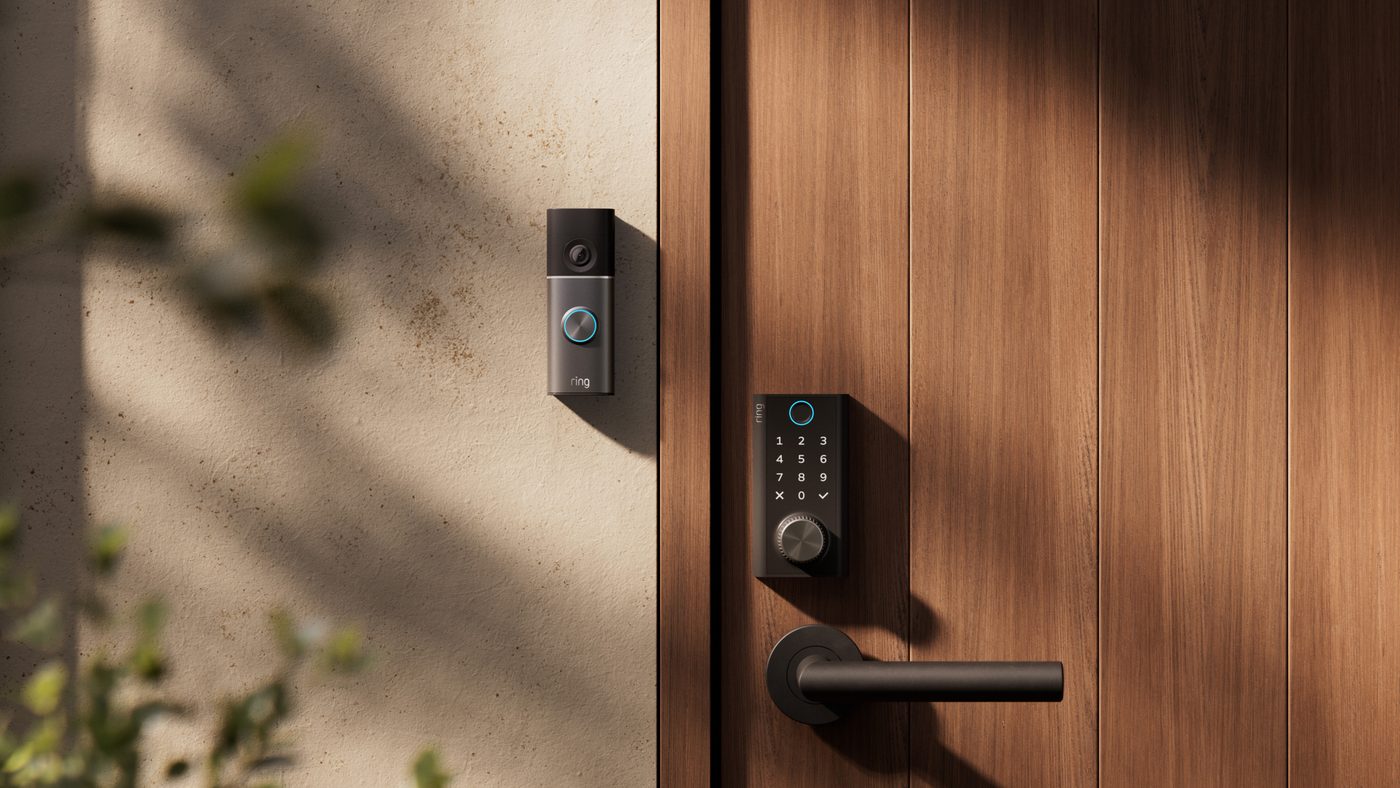 Ring Smart Lock on a wooden door with blue fingerprint ring, backlit keypad, and knurled Power Dial above the handle, with a Ring Video Doorbell beside it