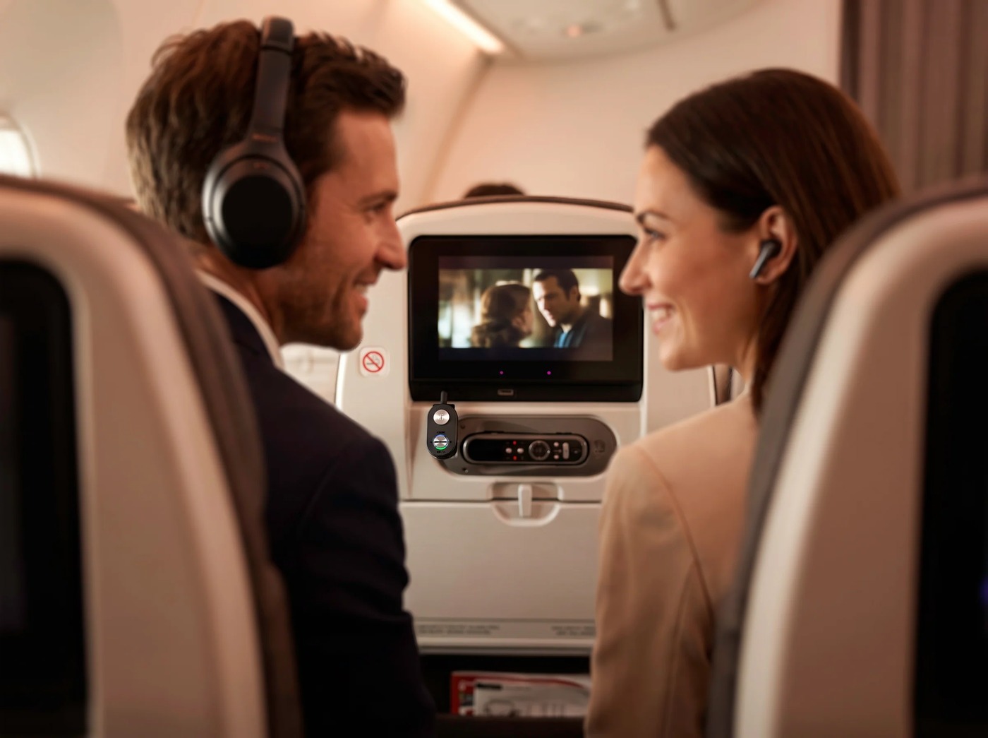 Two passengers share an in-flight film, each with their own headphones.
