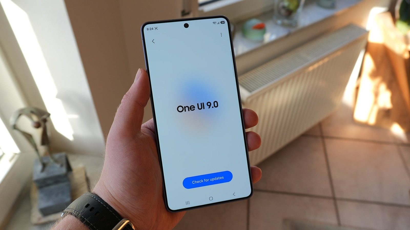 A Galaxy phone in hand showing the One UI 9.0 update screen