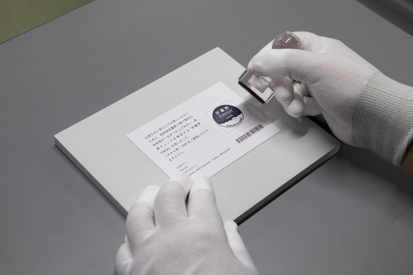 Gloved hands stamping an Azumino FINISH quality card at VAIO’s factory