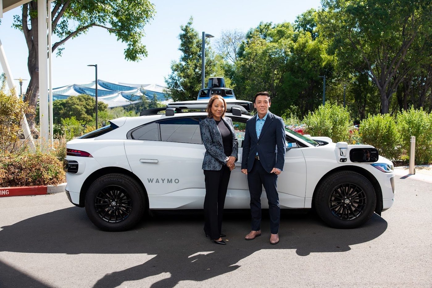 Two officials pose beside a Waymo Jaguar I-PACE