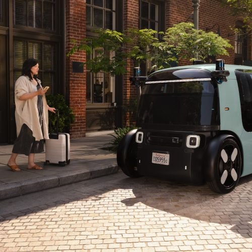A traveler with a suitcase stands beside a Zoox robotaxi